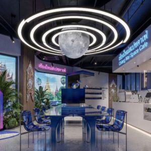Large glowing moon chandelier with LED rings hanging over a blue communal table in a space-themed cafe in Chiang Mai